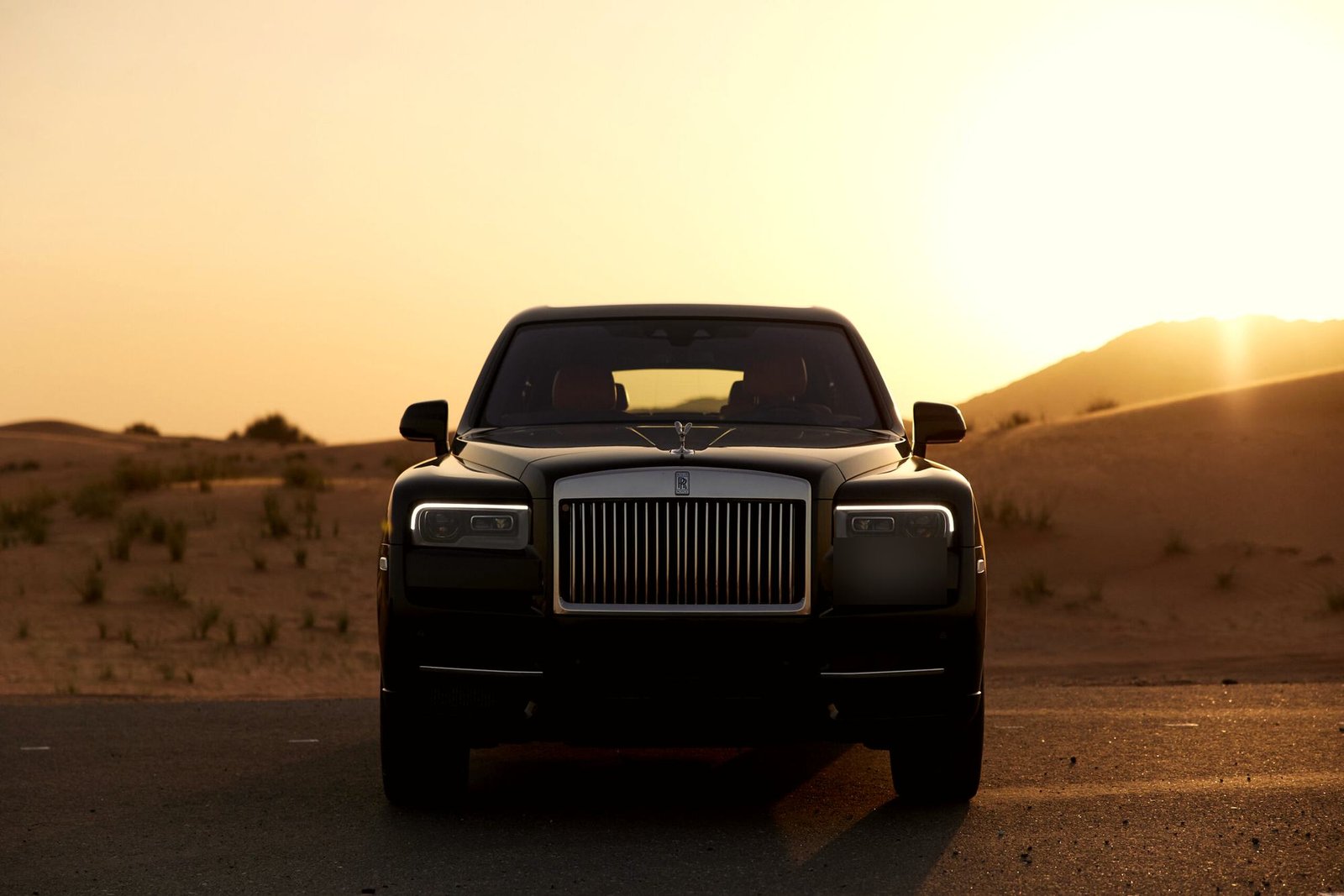 A black Rolls-Royce Cullinan in the desert at sunset